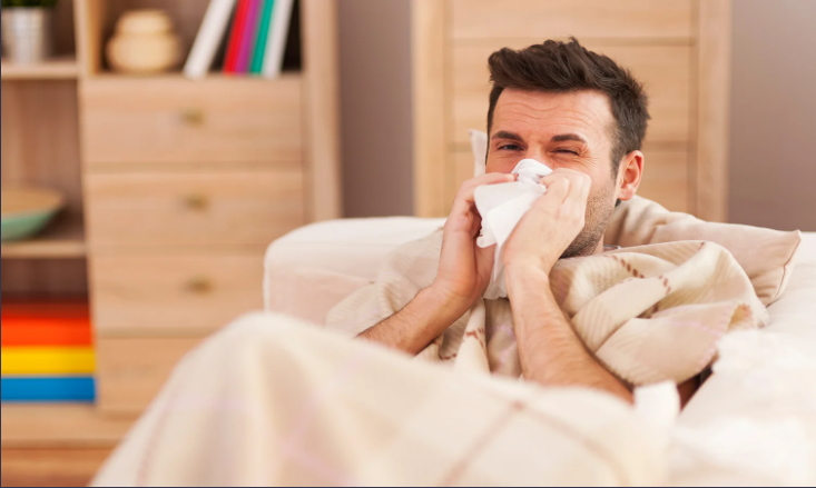 Sick man blowing his nose while wrapped in a blanket.
