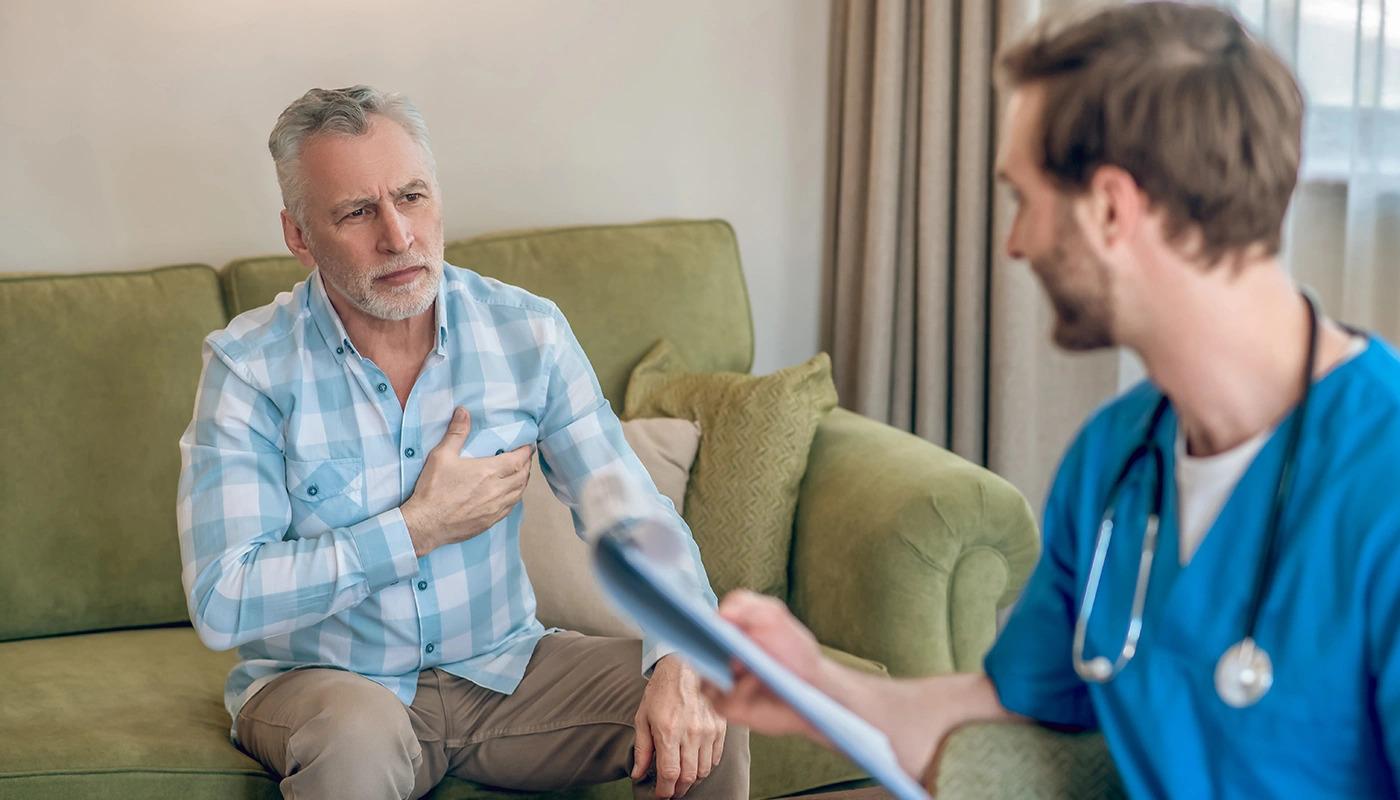 Senior man holding chest in pain while consulting doctor indoors.
