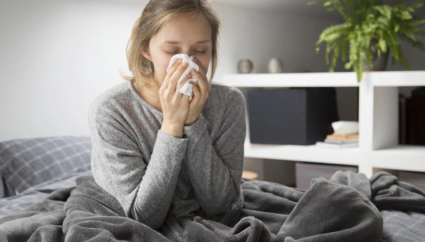 Sick woman sitting in bed and blowing her nose gently.