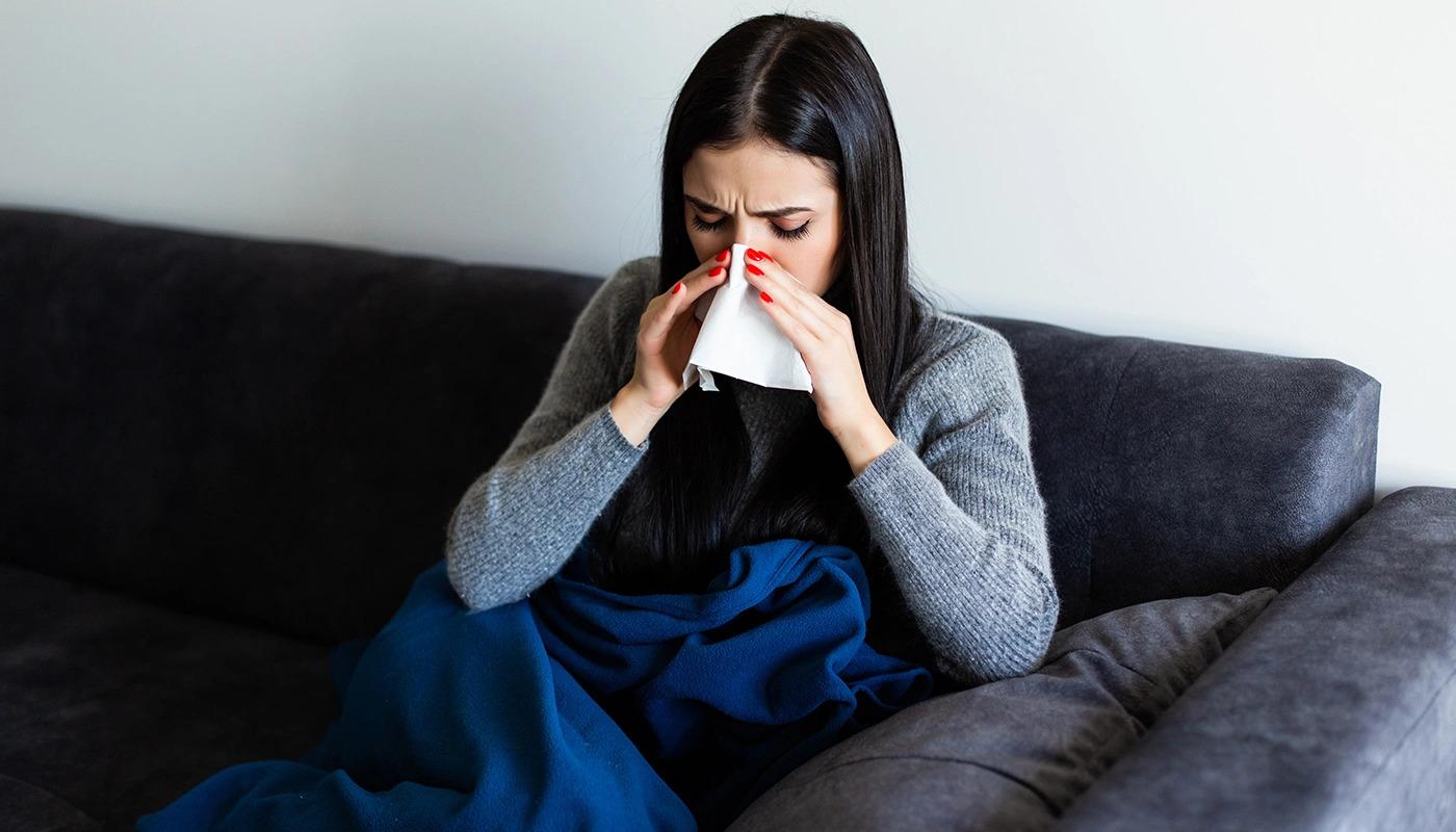 Woman wrapped in blanket blowing her nose with white tissue.