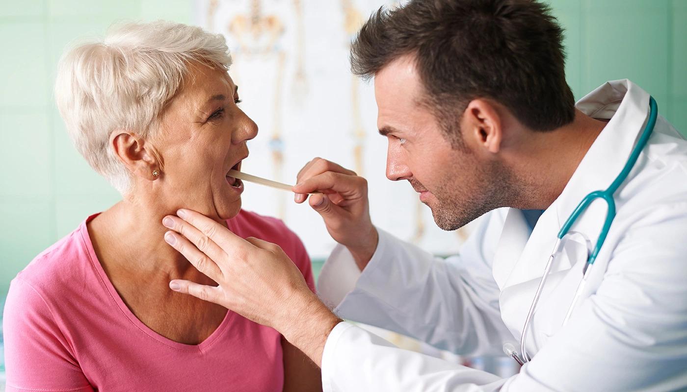 Doctor checking an older female patient's throat using a depressor.